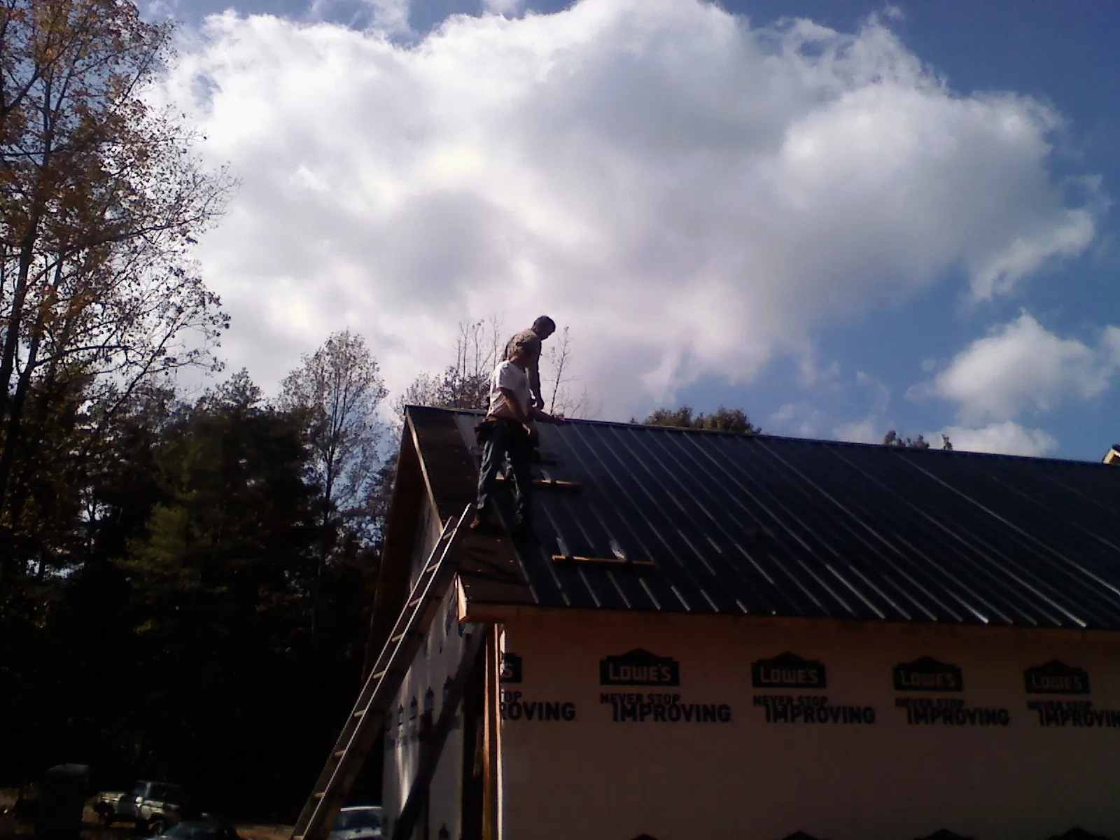 Roofer fastening dark metal panels high against a cloudy sky, from a Roof Inspection job in Elgin